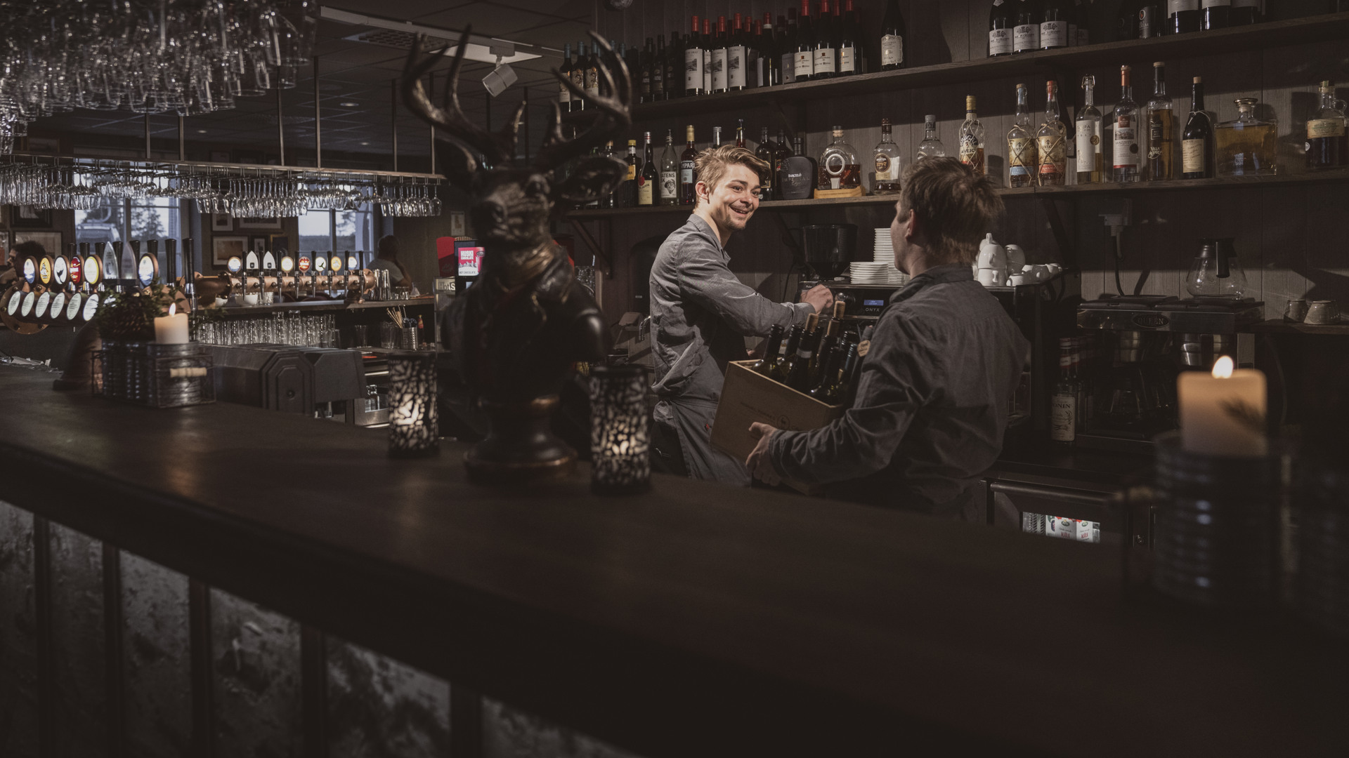 En bartender plockar bland flaskorna bakom disken samtidigt som han talar med en kollega