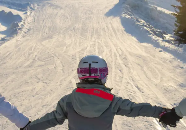 Three skiing girls hold each other's hands as they ski down Lämmeltåget